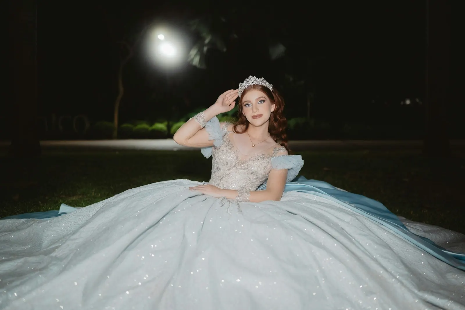 Quinceañera sentada en el pasto con su vestido extendido