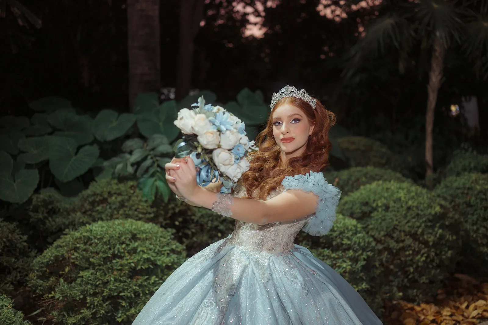 Quinceañera con vestido azul y ramo de flores en un jardín